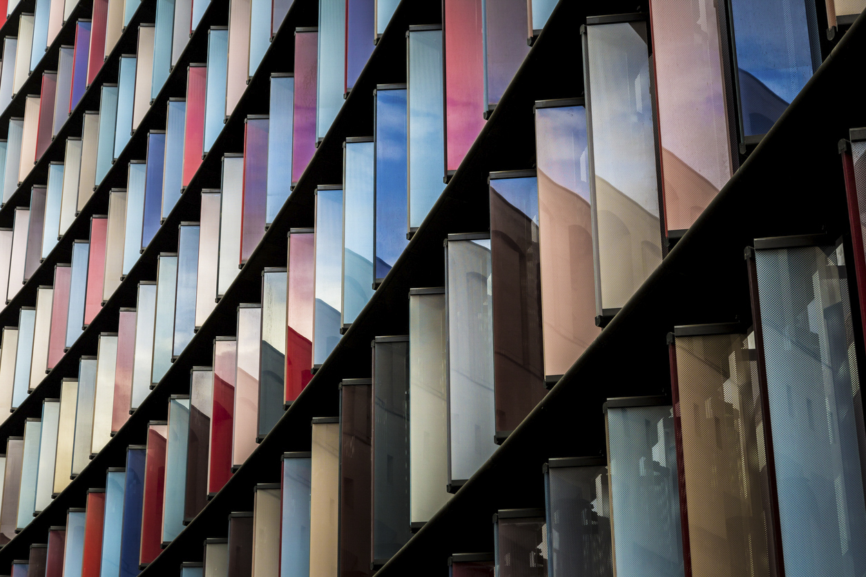 Abstract close up image looking up at contemporary architecture in London, UK. The office building exterior is composed of vibrant coloured glass which reflects the blue sky and cloudscape above. Horizontal colour image. 